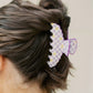 Person with a bun wearing a decorative purple and yellow hair clip on a plain background
