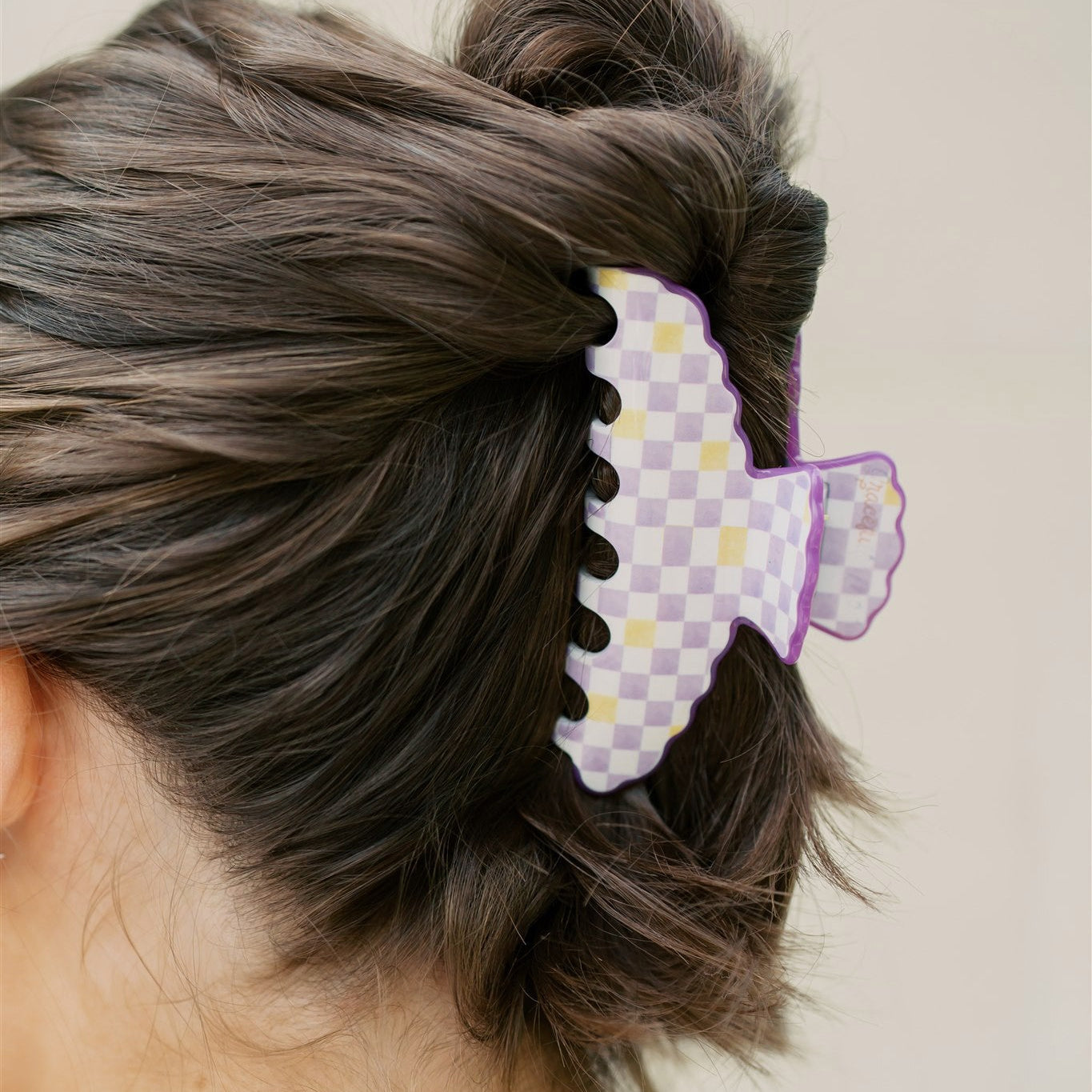 Person with a bun wearing a decorative purple and yellow hair clip on a plain background