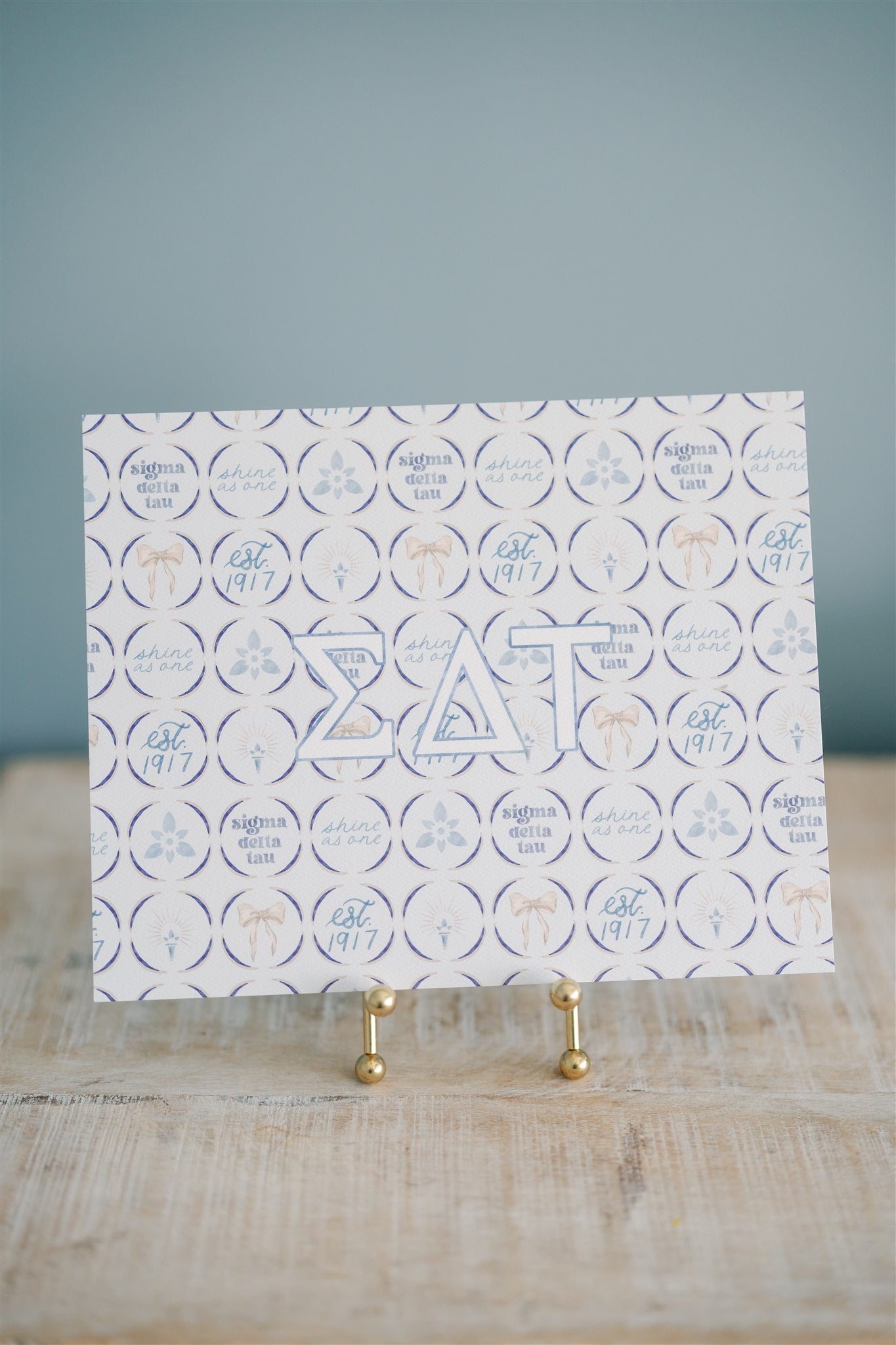 Decorative art print with circular designs and Sigma Delta Tau Greek letters on a stand against a blue background.