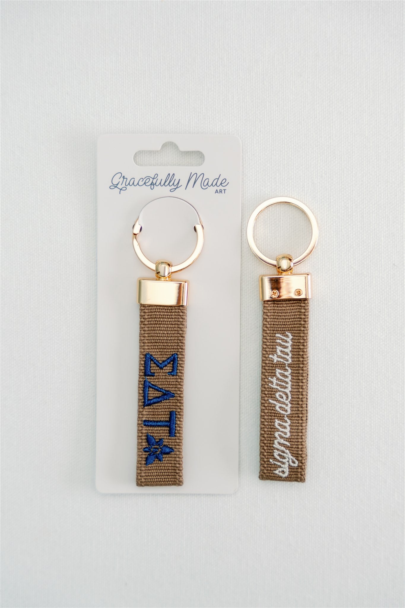 Front and back of the Sigma Delta Tau embroidered keychain with Gracefully Made Art branded packaging. 
