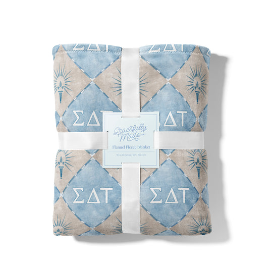 Folded blanket with geometric pattern and 'Sigma Delta Tau' symbols on a white background