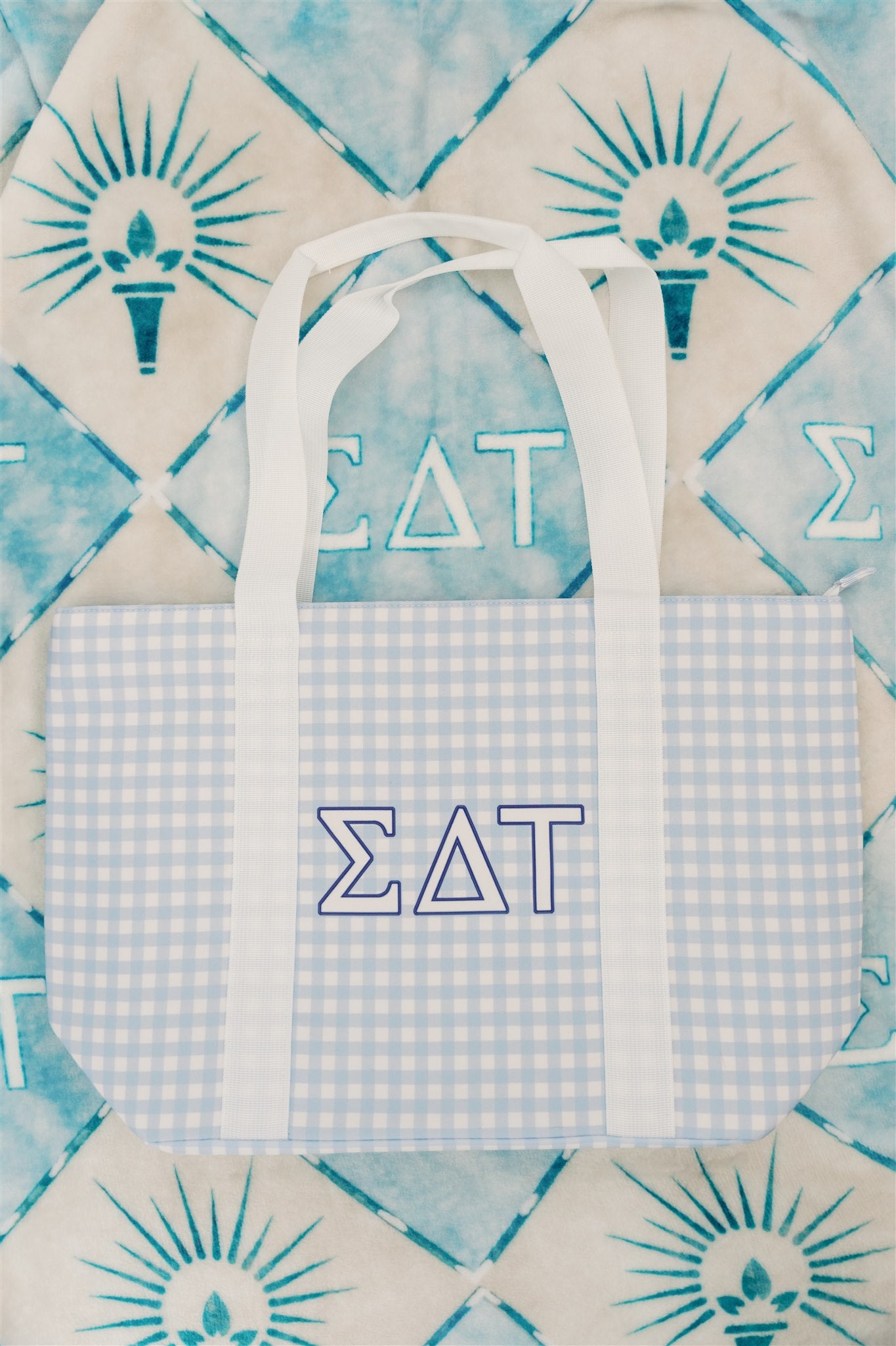 Blue checkered tote bag with white handles and Sigma Delta Tau Greek letters on a patterned background.