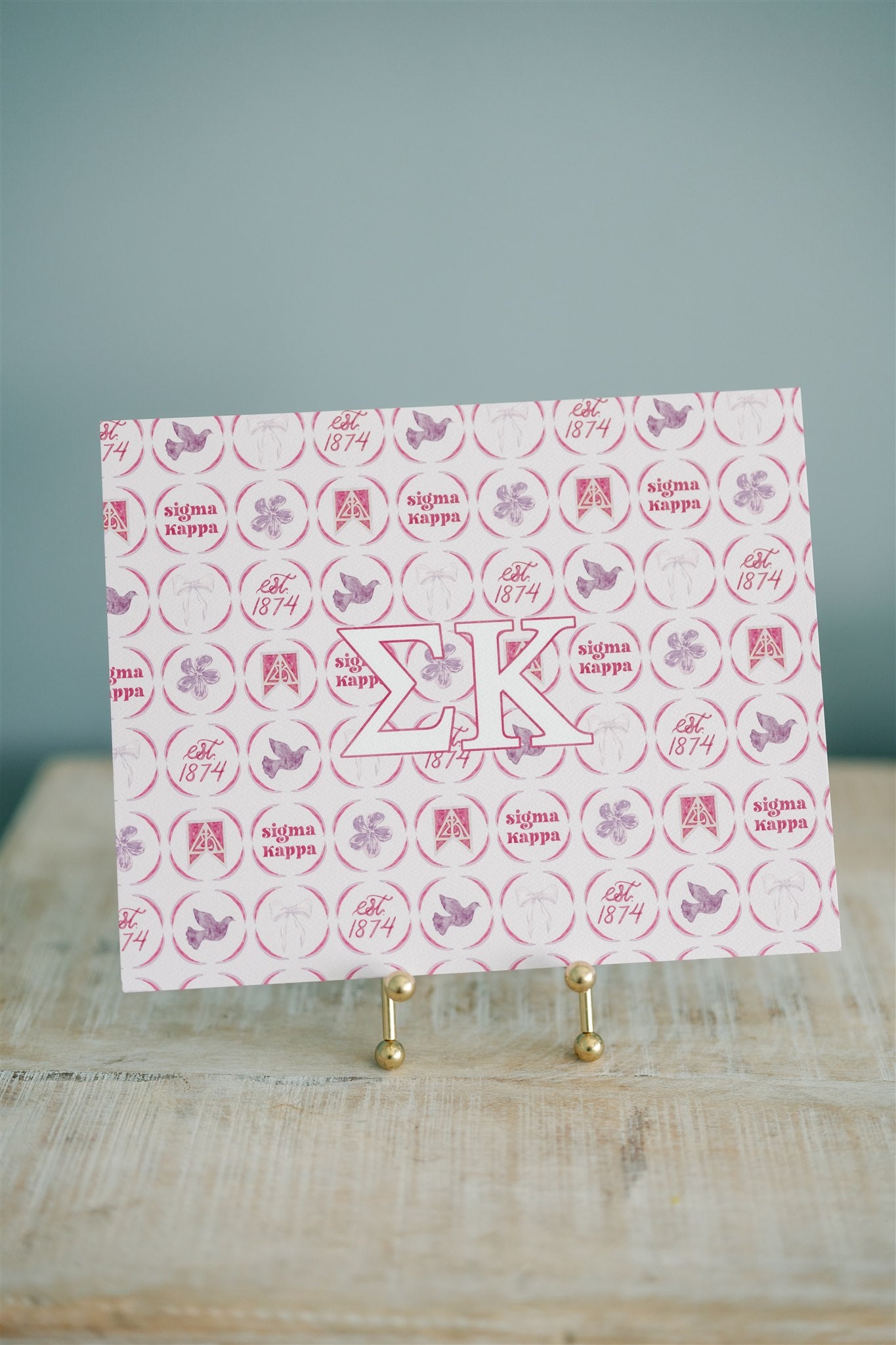 Decorative art print with 'Sigma Kappa' design and Greek letters on a stand against a blue background