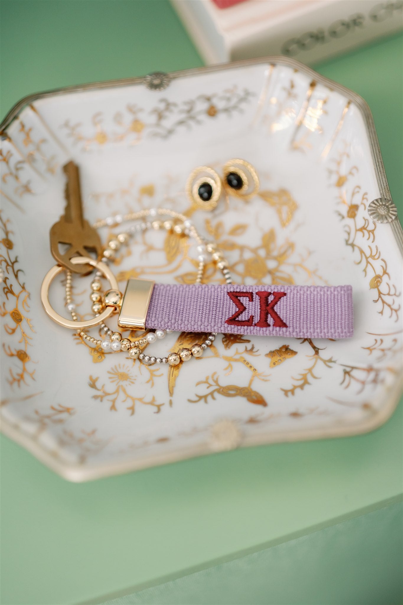Purple keychain embroidered with Sigma Kappa Greek letters sitting on a jewelry dish.
