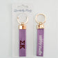 Front and back of a purple keychain with Sigma Kappa embroidered on it in Gracefully Made Art branded packaging. 