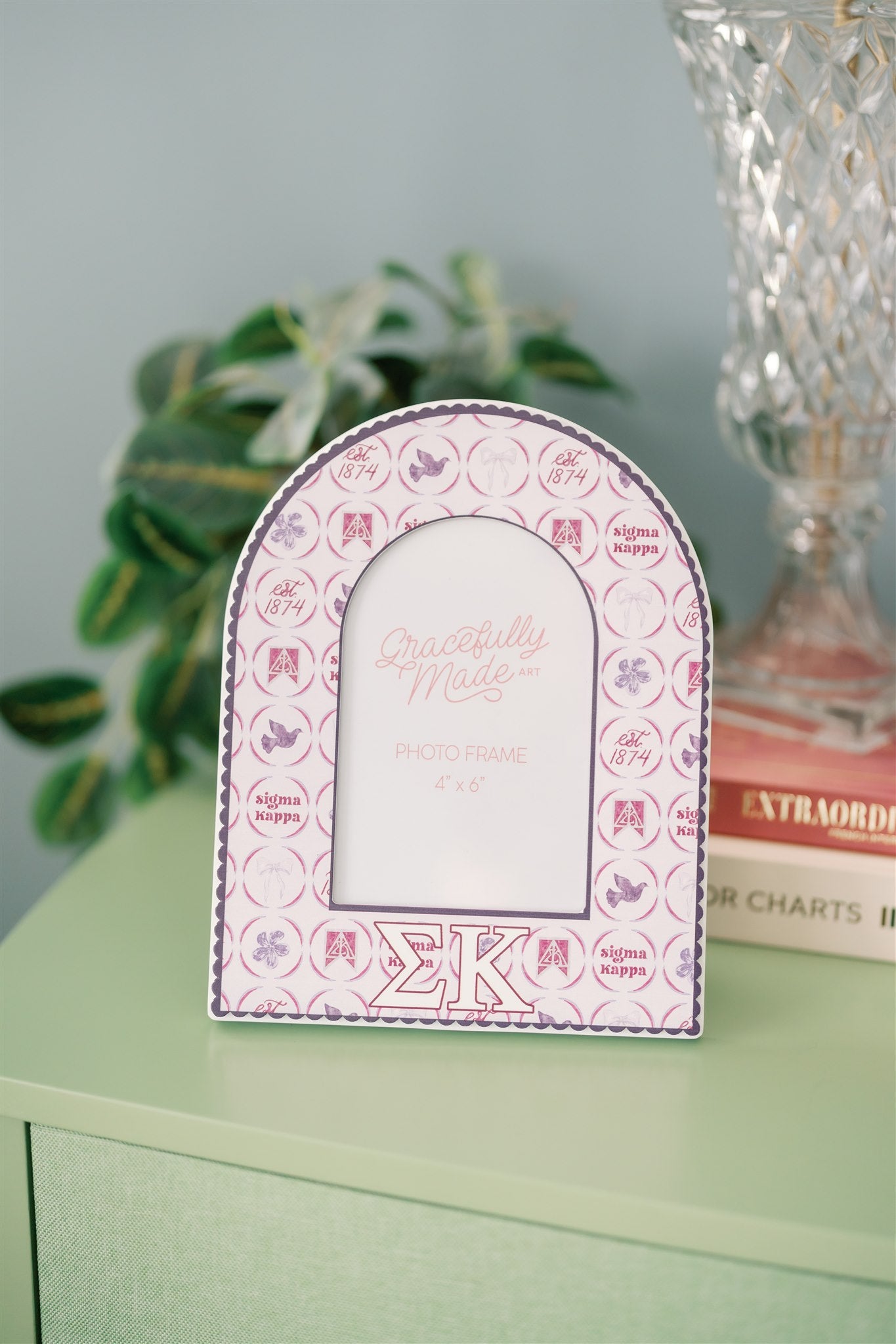 Decorative photo frame with pink and white design and Sigma Kappa Greek letters on a green dresser.