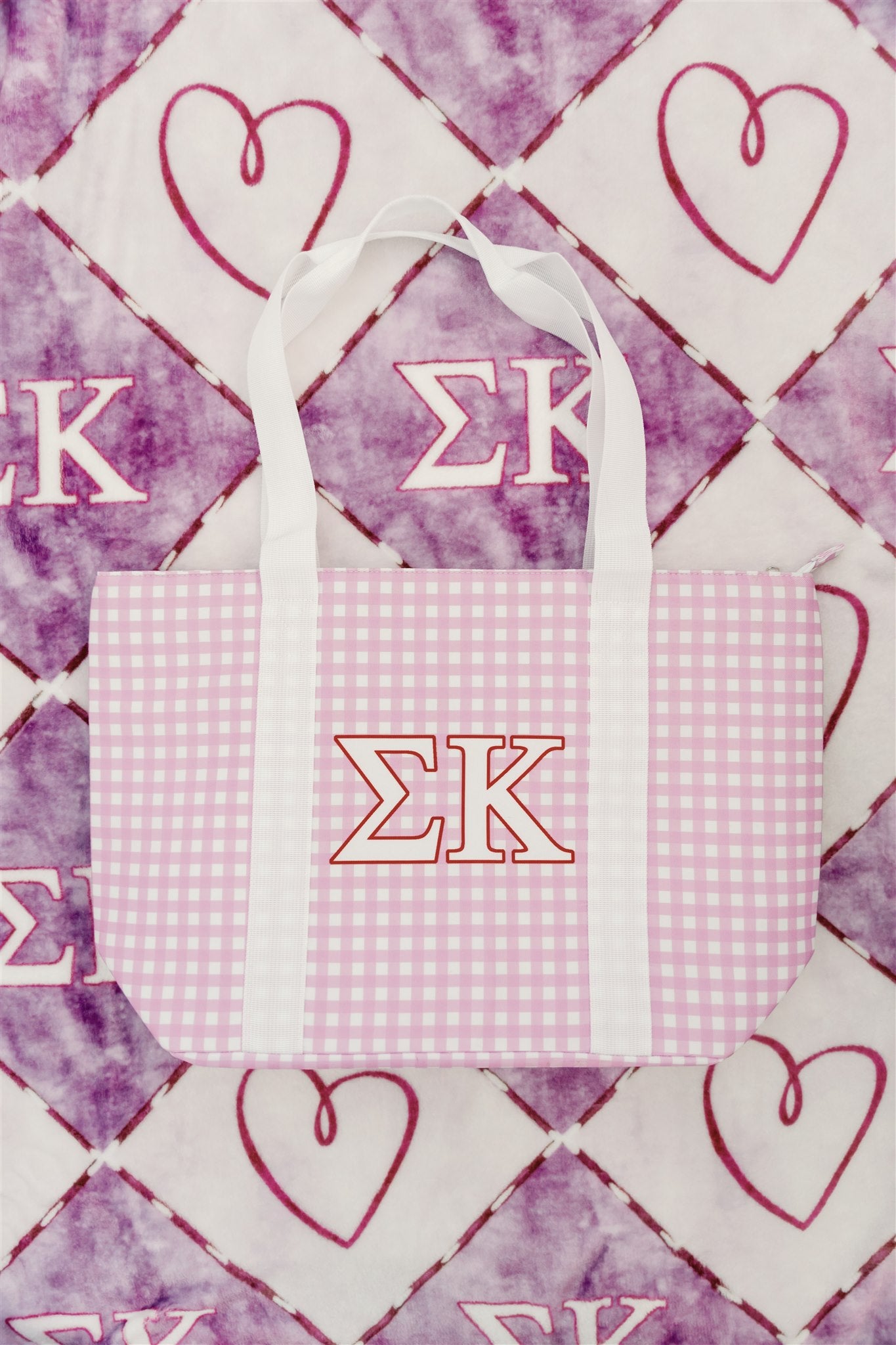 Purple gingham tote bag with white handles and Sigma Kappa Greek letters on a patterned background