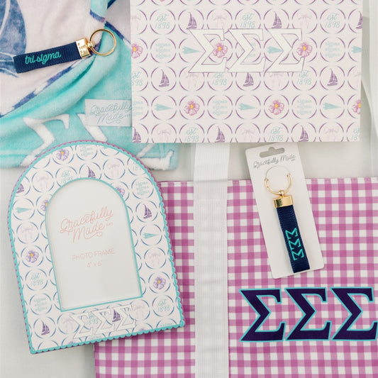 Collection of Tri Sigma decorative items including an art print, keychain, and checkered tote bag on a light gray background.
