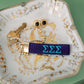 Blue keychain with Tri Sigma Greek letters embroidered on it set on a jewelry dish.