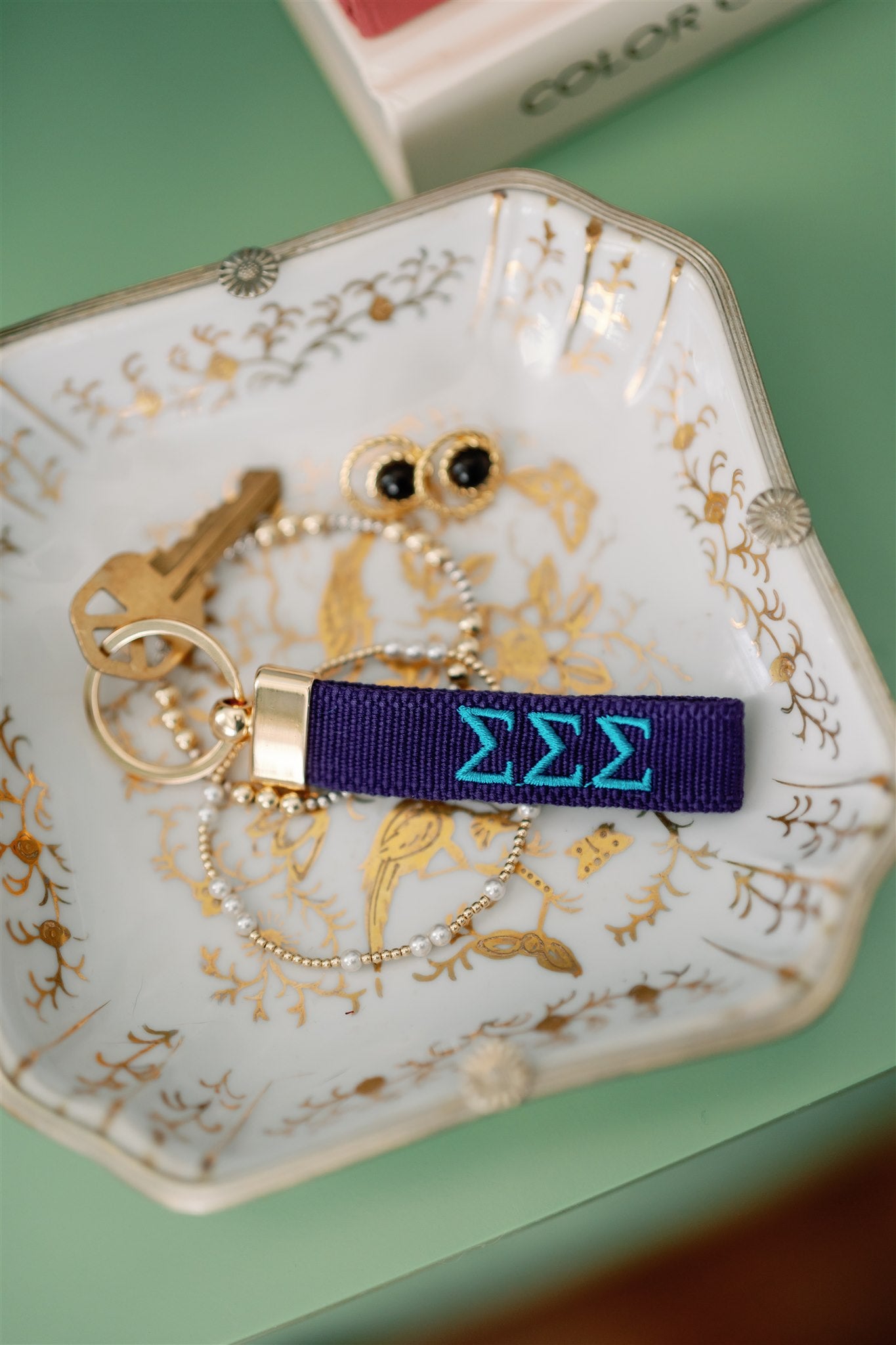 Blue keychain with Tri Sigma Greek letters embroidered on it set on a jewelry dish.