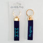 Front and back of a blue keychain with Tri Sigma embroidered on it in Gracefully Made Art packaging. 