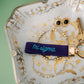 Decorative dish with jewelry including a key, bracelet, and 'tri sigma' keychain on a green background.