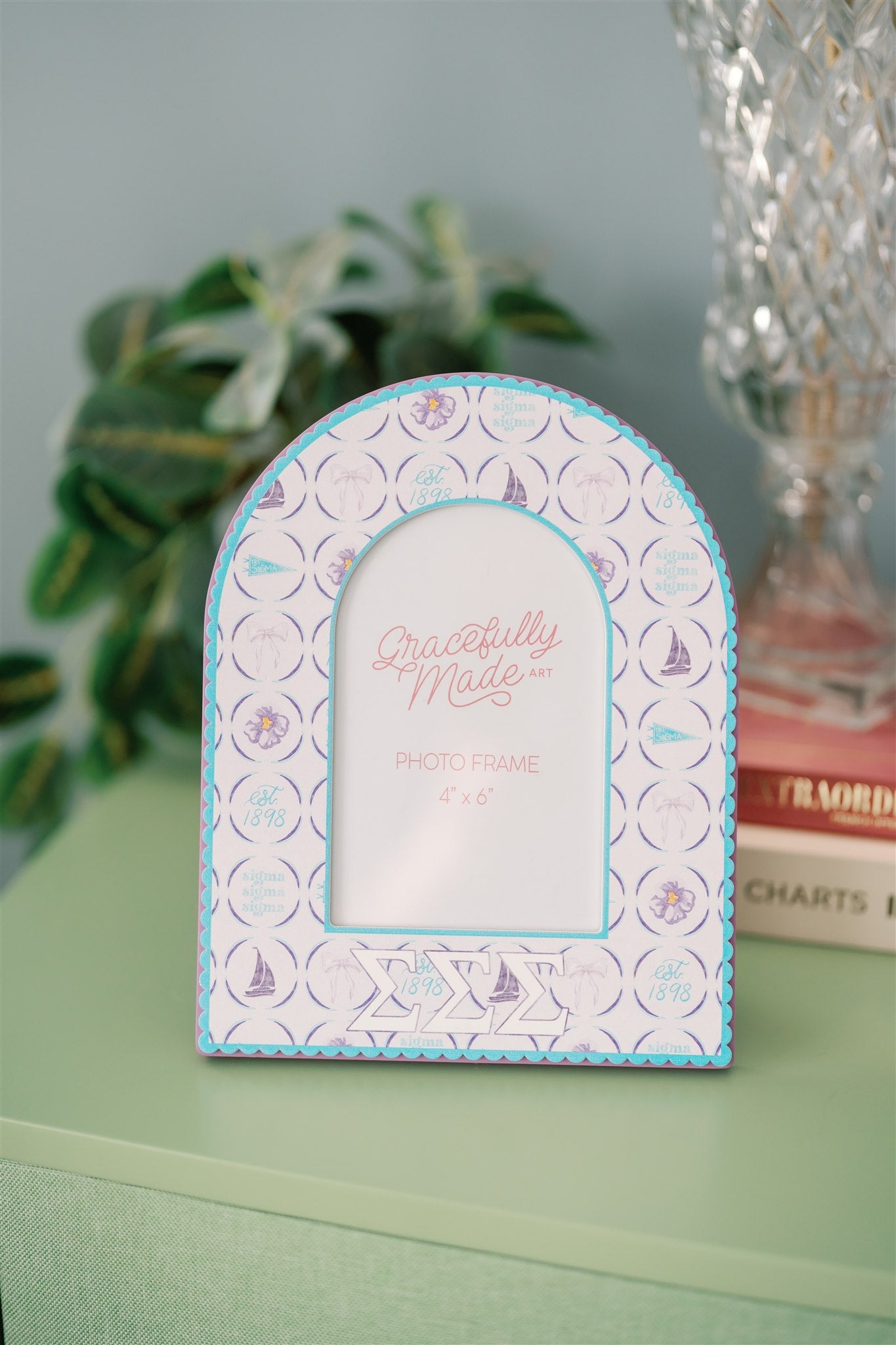 Decorative photo frame with Tri Sigma pattern and Greek letters on a green dresser.