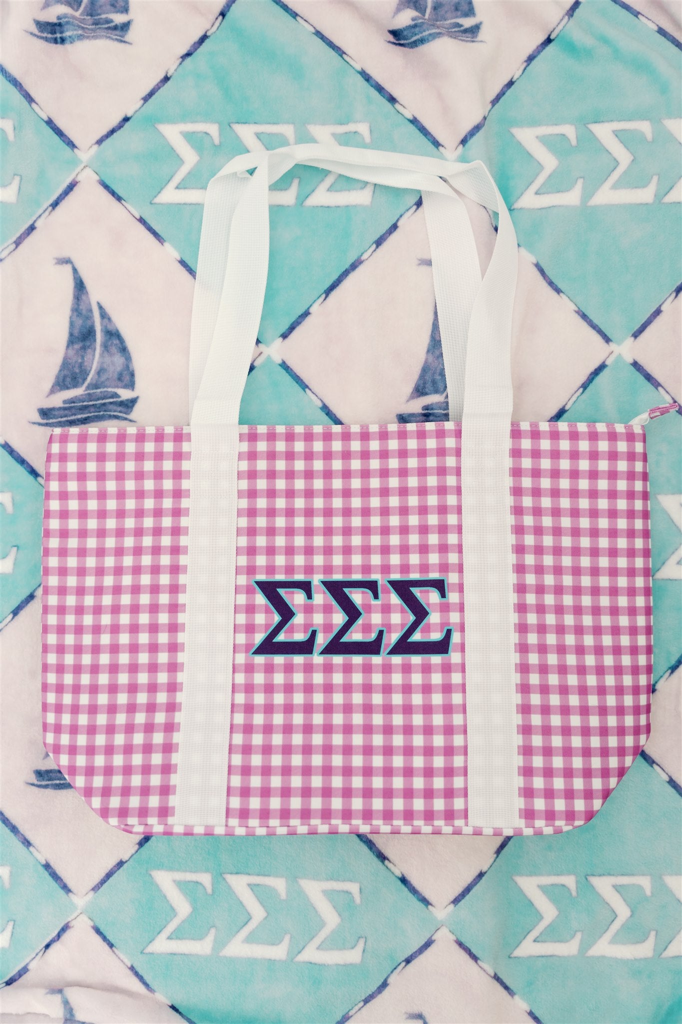 Purple gingham tote bag with blue Tri Sigma Greek letters on a patterned background