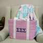 Purple gingham tote bag with blue Tri Sigma Greek letters propped on a green chair