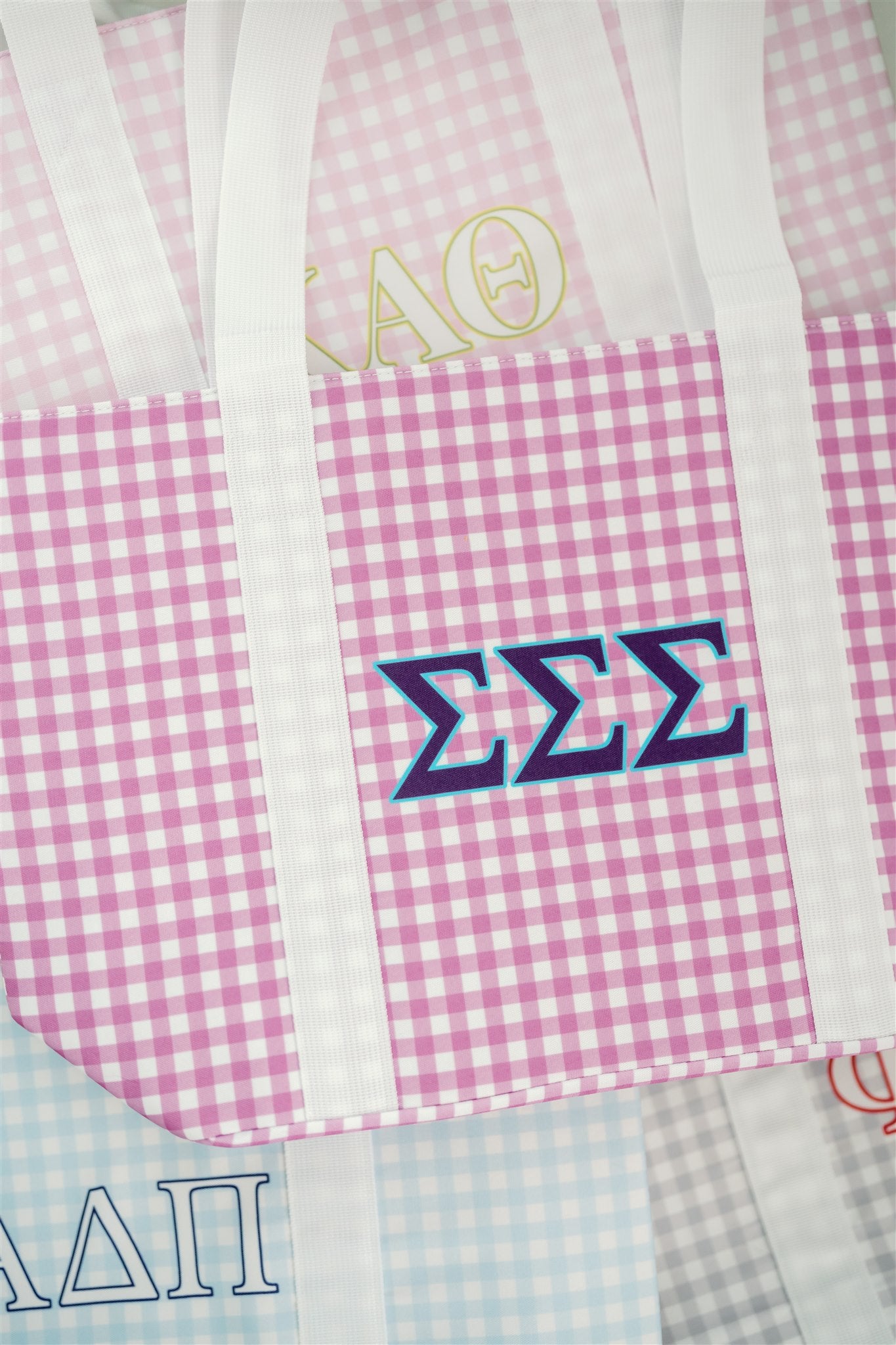 Close up of the Tri Sigma tote bag with a Greek letters, purple gingham pattern, and white handles.