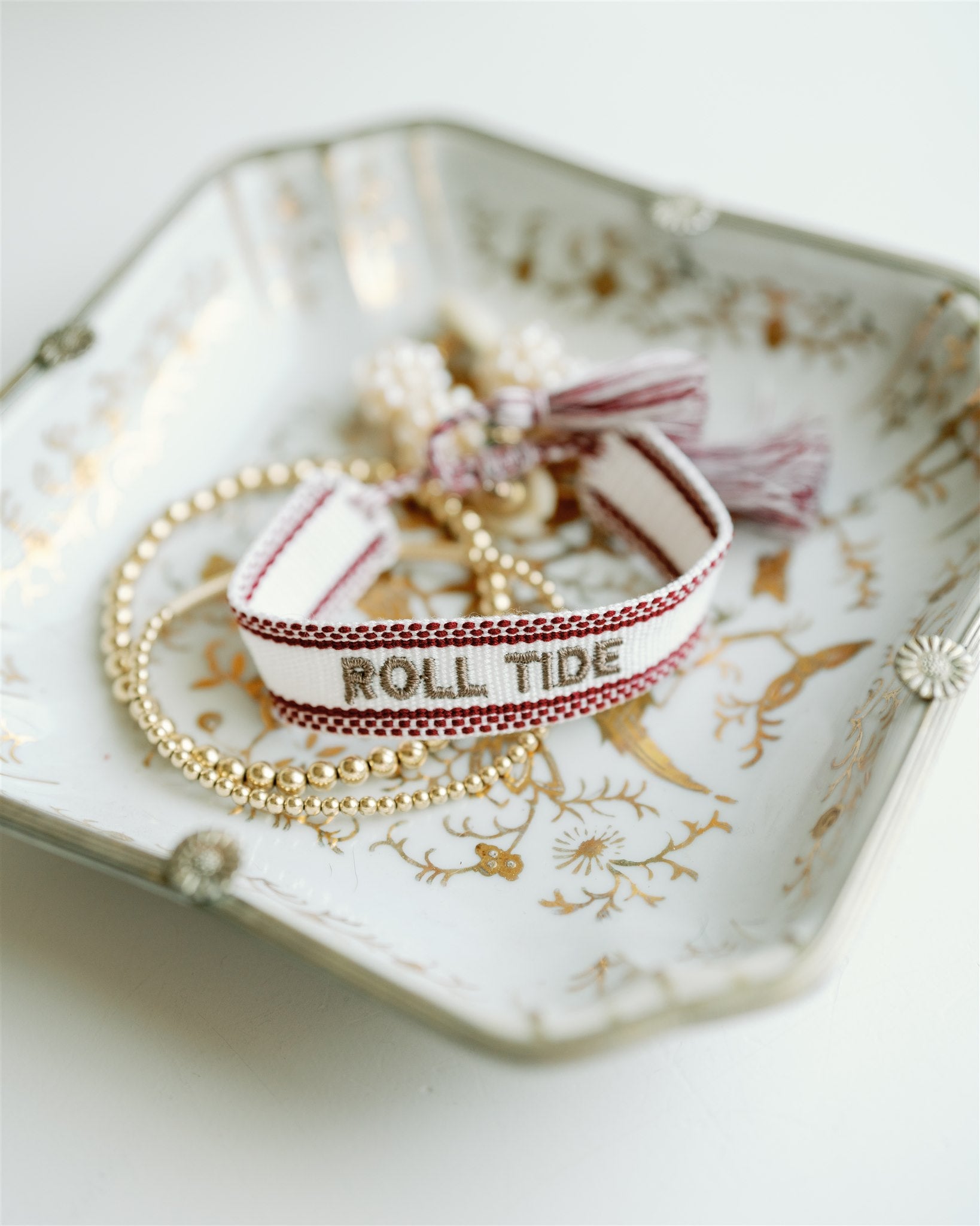 White and red woven bracelet with "Roll Tide" written down the middle.
