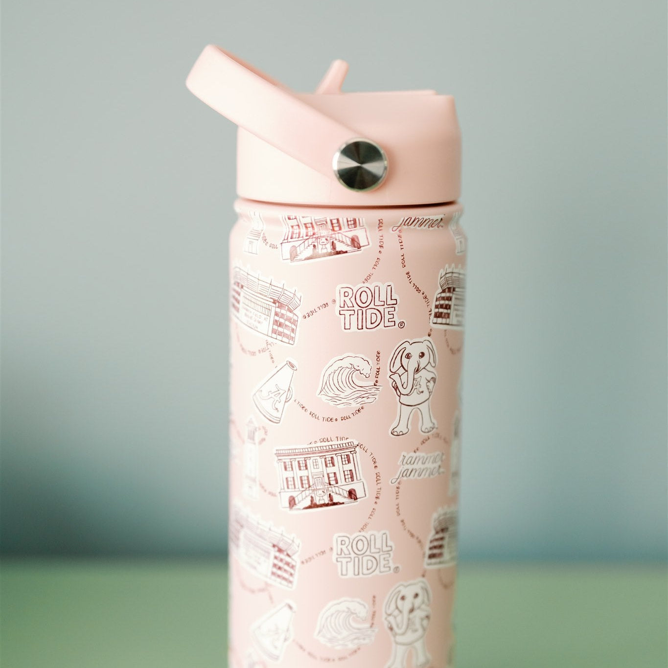 Light red water bottle with a University of Alabama pattern on a green surface and gray background