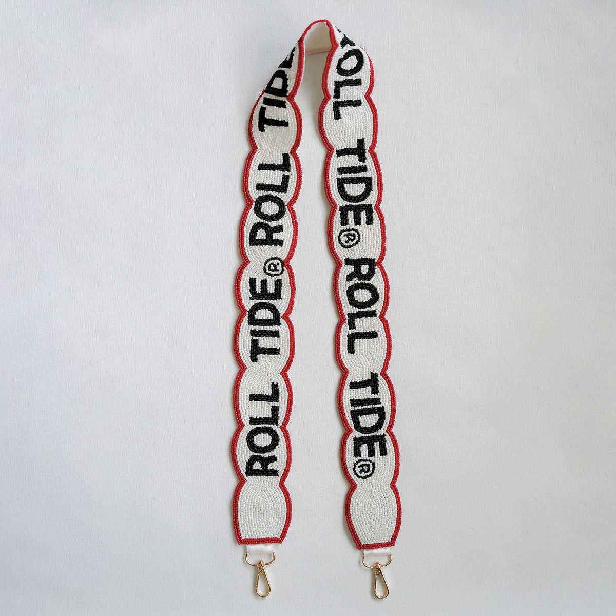 A white beaded strap with scalloped edges, featuring 'ROLL TIDE' in black with a red outline, finished with gold-tone metal clasps at the bottom, laid flat on a white background.