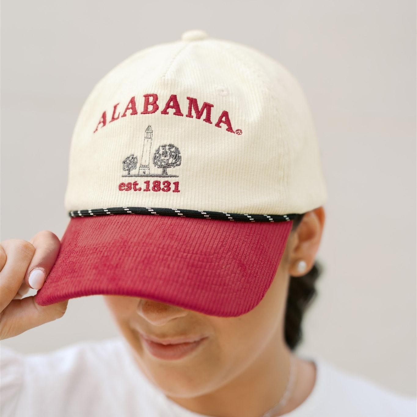 Person wearing a white and red 'Alabama' cap with text on a plain background
