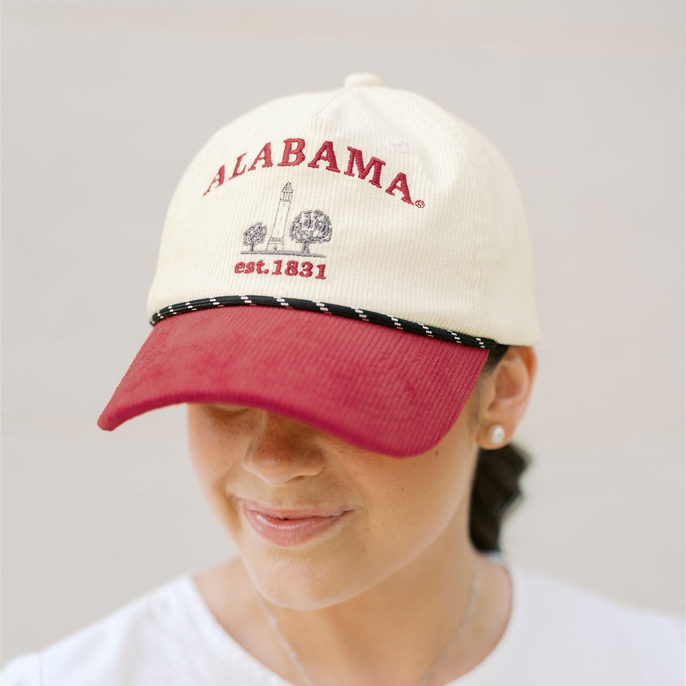 Person wearing a white and red 'Alabama' cap on a plain background