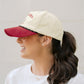 Woman wearing a beige cap with a red brim and 'Alabama' text on a plain background