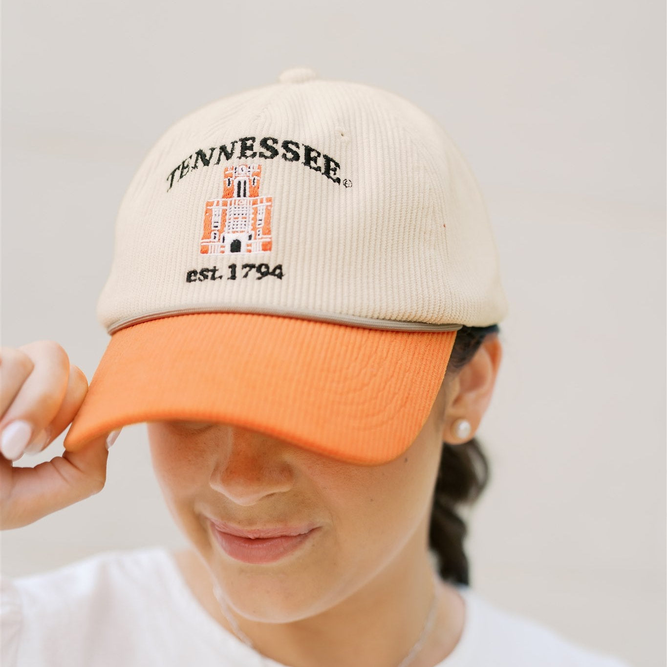 Person wearing a beige and orange baseball cap with 'Tennessee' text on a plain background