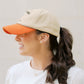 Person wearing a beige cap with an orange bill against a plain background