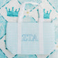 ZTA tote bag with blue gingham pattern, white handles, and Greek letters on a patterned background.